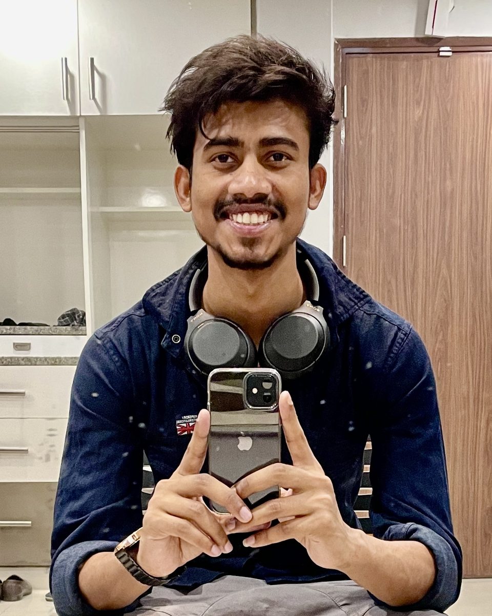 Adarsh Chaudhary, smiling, with headphones around his neck